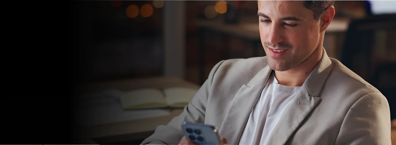 Man in a light blazer smiling while looking at his smartphone in a cozy cafe setting.