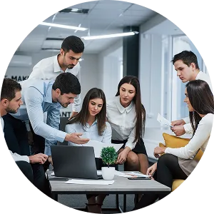 Group of six coworkers gathered around a laptop on a coffee table, collaborating in a modern office.
