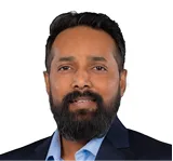 Portrait of a man with a full beard in a dark blazer and light blue shirt, facing the camera.