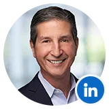 Professional headshot of a smiling man in a dark blazer, with a LinkedIn badge overlaid on the image.
