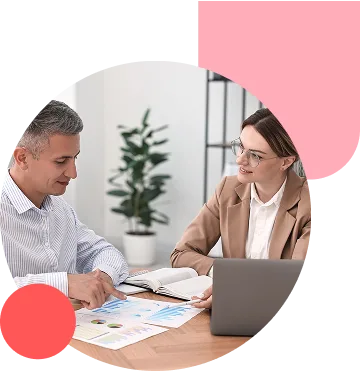Two professionals in a bright office review documents and charts on a table, with a laptop nearby.