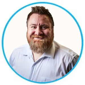 Smiling man with a beard in a light blue button-down shirt, portrait framed by a blue circular border.
