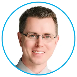 Professional headshot of a smiling man with short dark hair and glasses, wearing a light blue shirt, framed by a blue circular avatar border.