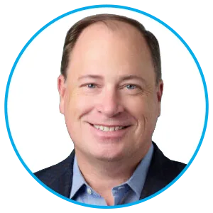 Head-and-shoulders portrait of a smiling man wearing a blue shirt and navy blazer, against a white background within a circular blue frame.