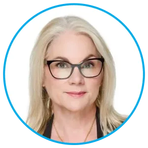 Portrait of a blonde woman with black glasses looking at the camera, wearing a dark top.