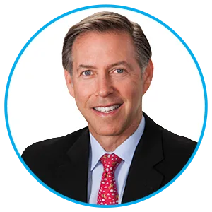 Professional headshot of a smiling middle-aged man in a dark suit and pink tie, inside a blue circular frame.