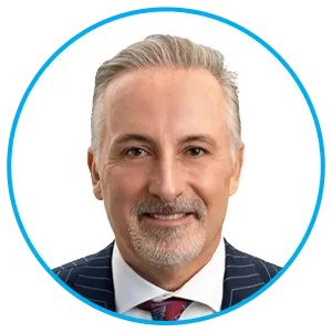 Portrait of a middle-aged man with silver hair and a trimmed beard, wearing a dark pinstripe suit and red tie, smiling at the camera.